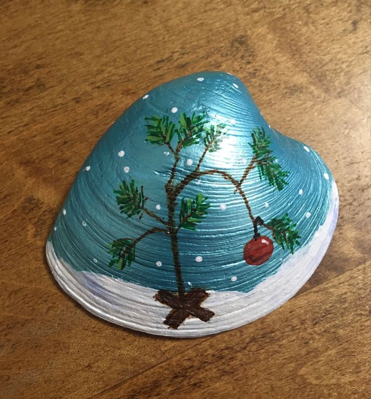 a painted rock on a wooden table with snow and christmas tree decorations in the top