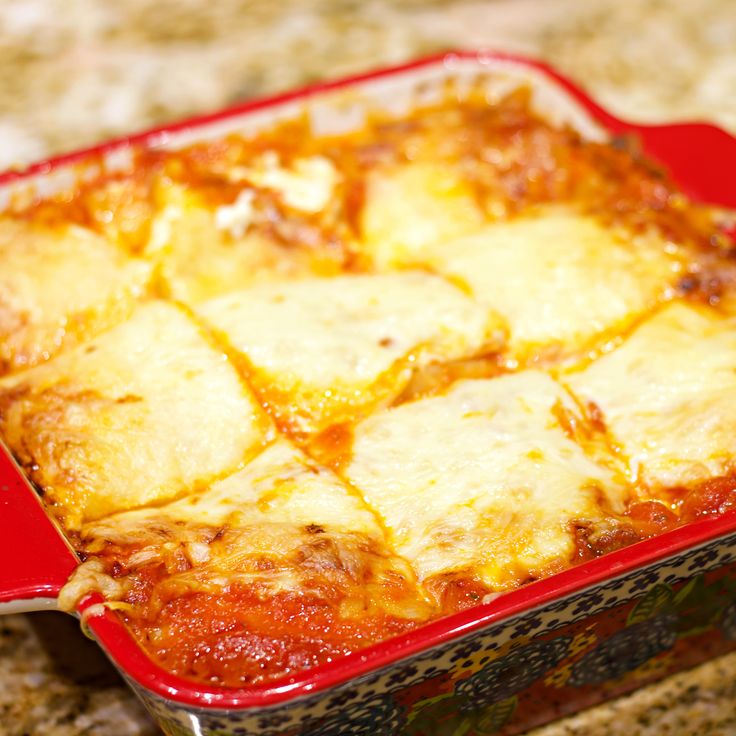 a red casserole dish filled with lasagna and cheese on a counter