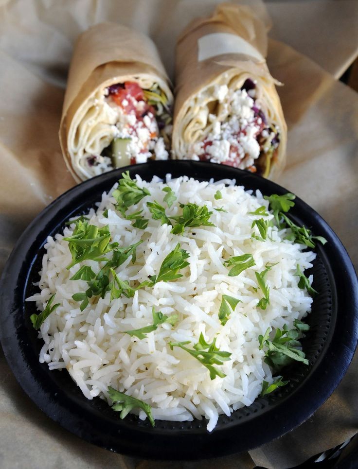 two burritos with white rice and garnishes in a black bowl