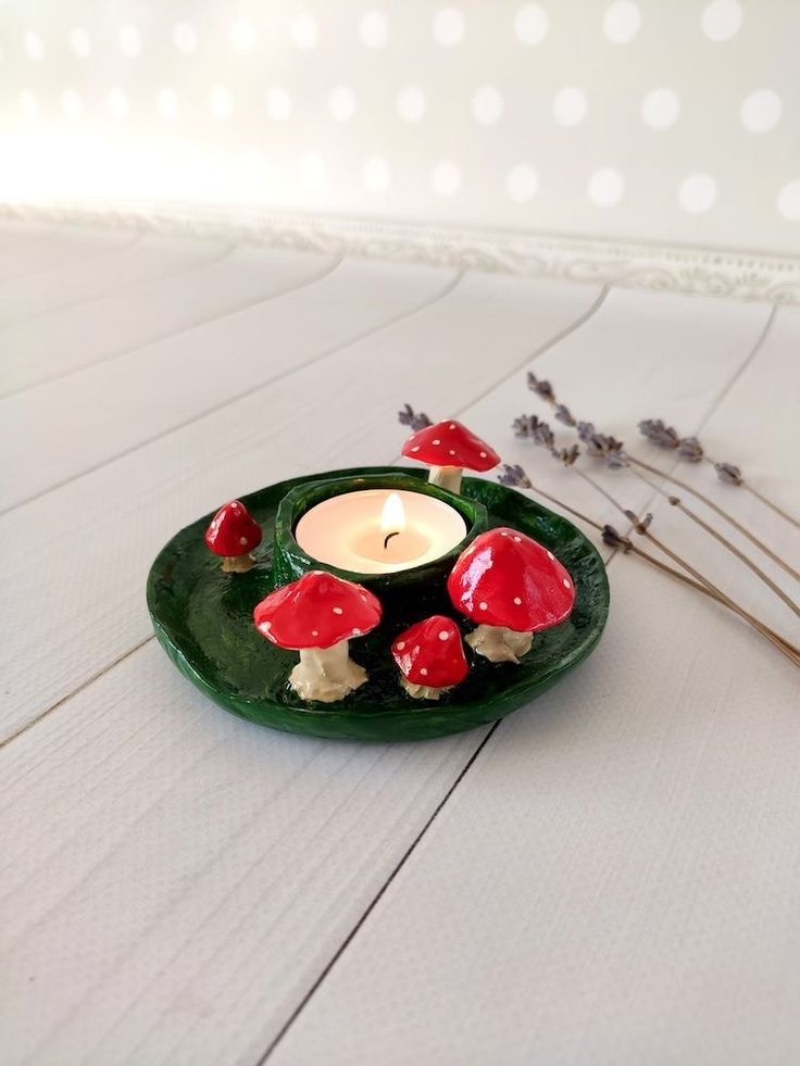 a green plate with red mushrooms on it and a lit candle in the middle sitting on a white table