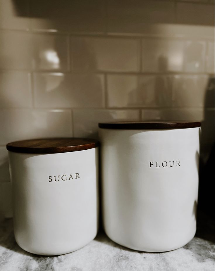 two white sugar jars sitting on top of a counter