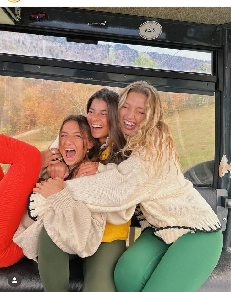 three girls are hugging each other in front of a window on a tour bus and smiling