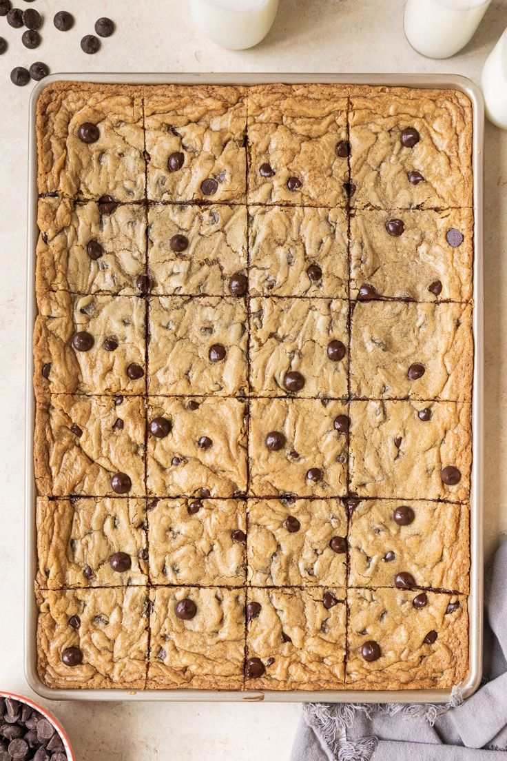 chocolate chip cookie bars on a baking sheet with milk and chocolate chips scattered around them