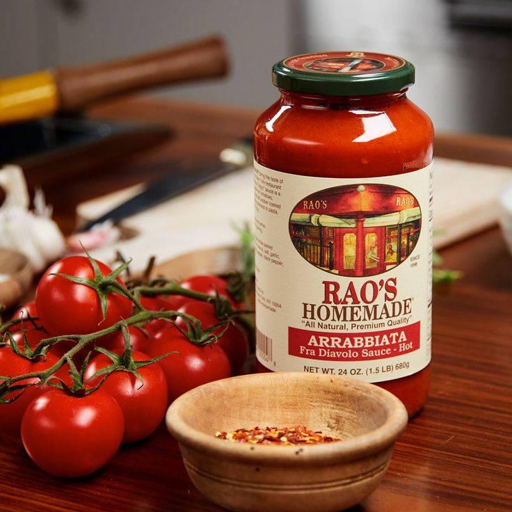 tomatoes and other vegetables sit on a table next to a jar of homemade tomato sauce