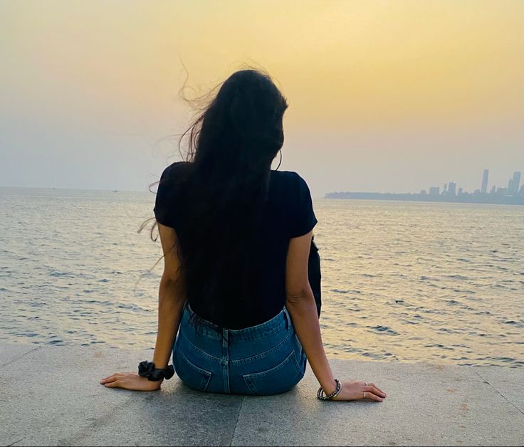 a woman sitting on the edge of a pier looking out at the water