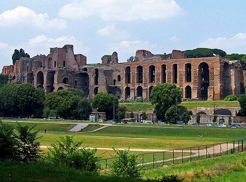 an old building in the middle of a lush green field with trees on both sides