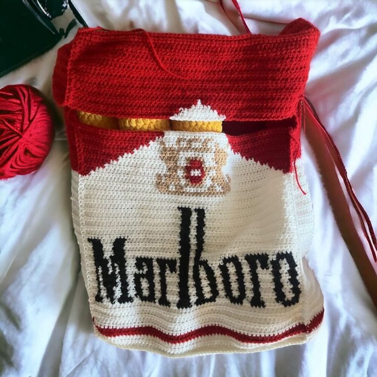 a crocheted bag sitting on top of a bed next to a ball of yarn