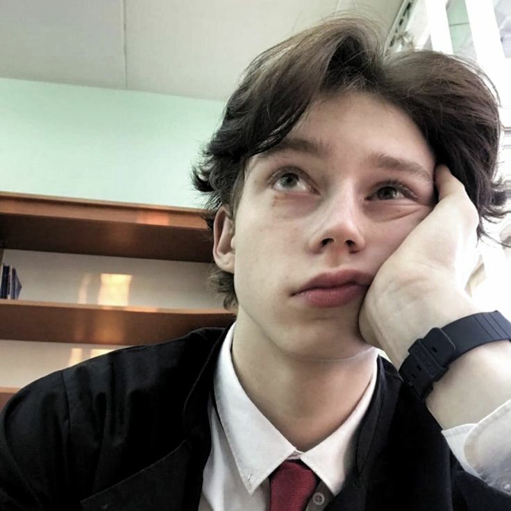 a young man wearing a suit and tie sitting in front of some stairs with his hand on his face