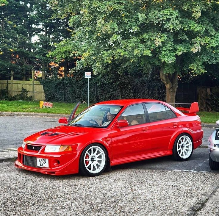 two cars parked next to each other in a parking lot with trees and bushes behind them