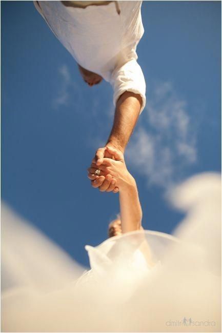 two people holding hands in the air with clouds around them and blue sky behind them