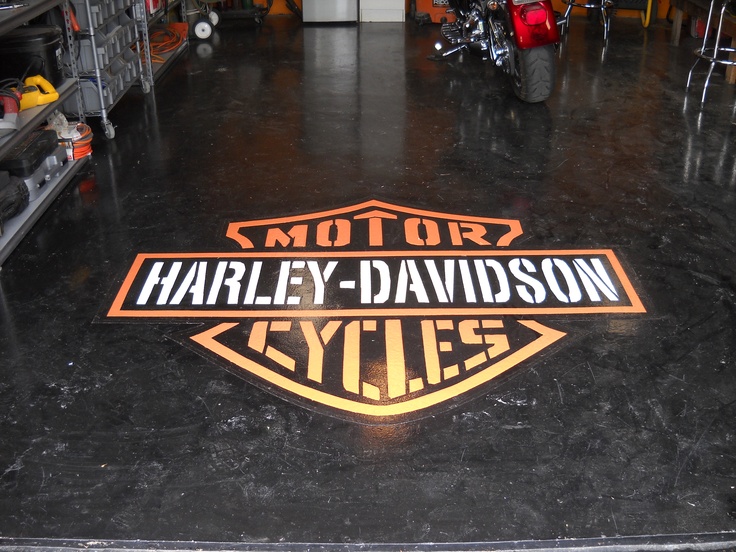 an orange and black harley davidson logo is on the floor in a garage with other motorcycles