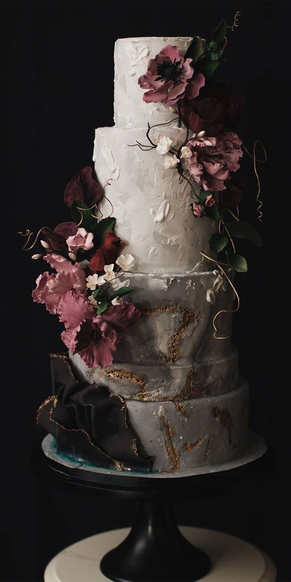 a three tiered white cake with flowers on the top and bottom, sitting on a black stand