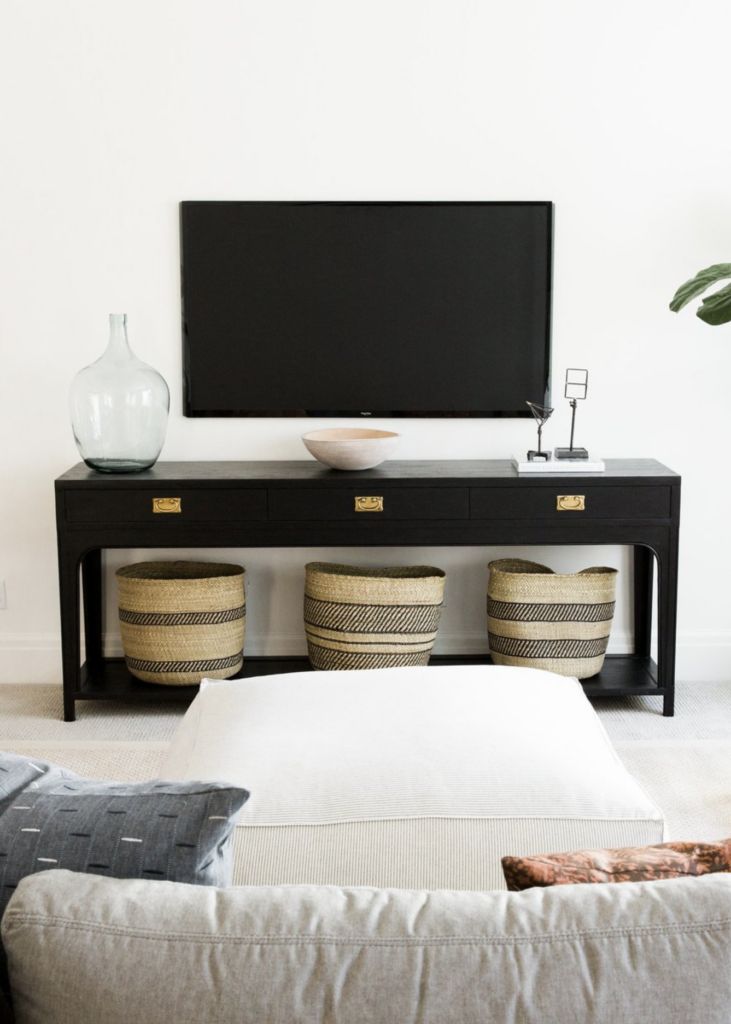 a flat screen tv mounted to the side of a wall above a table with baskets on it