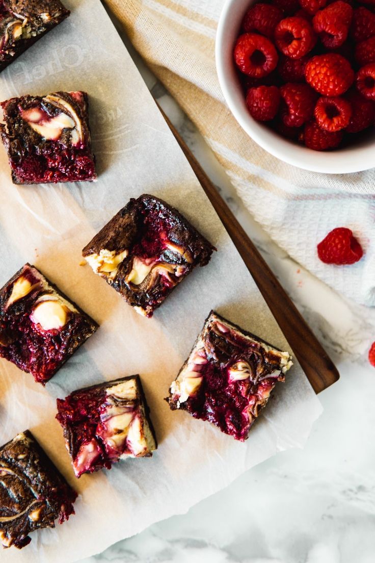 raspberry cheesecake brownies on parchment paper next to bowl of strawberries