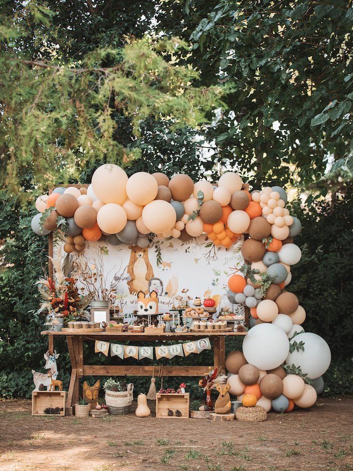 an outdoor party with balloons and decorations on the table, in front of some trees