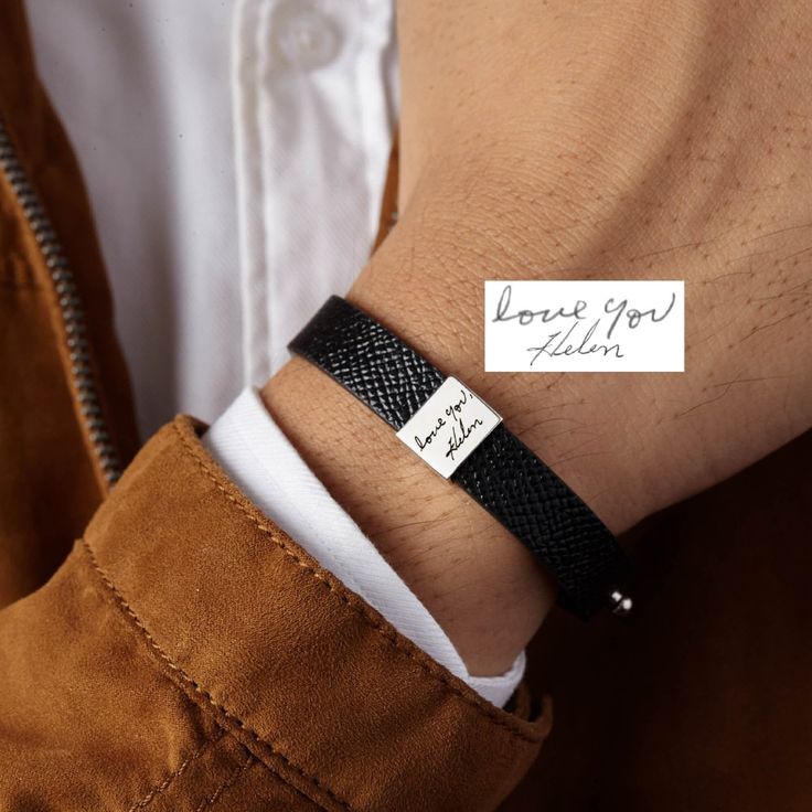 a man wearing a black leather bracelet with a note on it