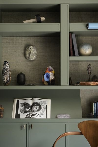 an open book shelf with books and vases on it, next to a chair