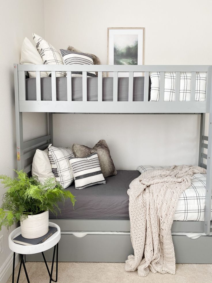 a bunk bed with pillows and blankets on it in a small room next to a potted plant