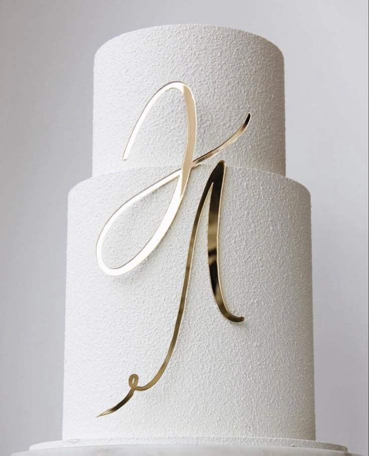 a white and gold wedding cake with the letter f on it's top tier