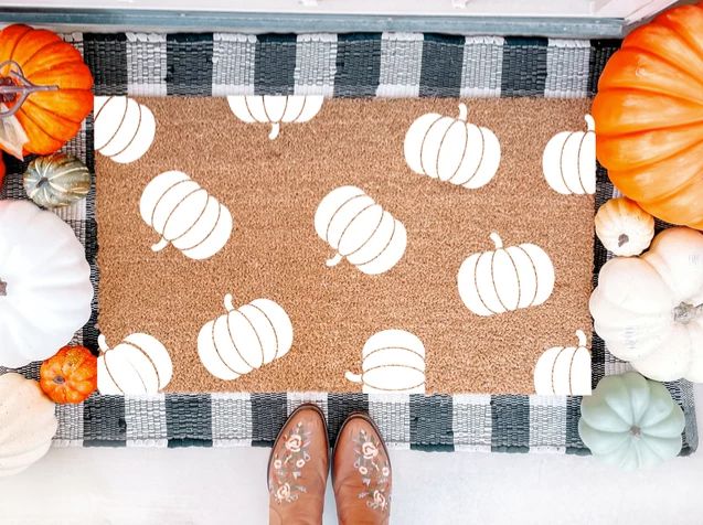 a person standing in front of a door mat with pumpkins on it