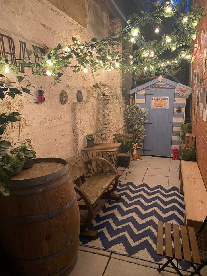 an outdoor area with wooden benches, potted plants and lights strung from the ceiling