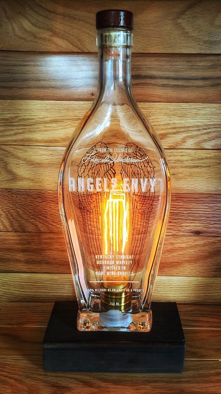 an empty glass bottle sitting on top of a wooden table next to a light bulb