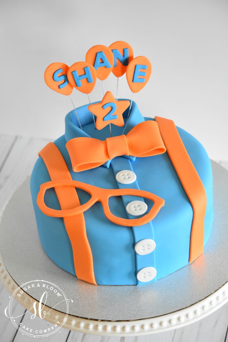 a blue and orange cake with an orange bow tie, name tag and glasses on top