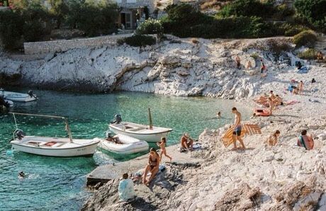 many people are on the beach and in the water near small boats that are tied up to the shore