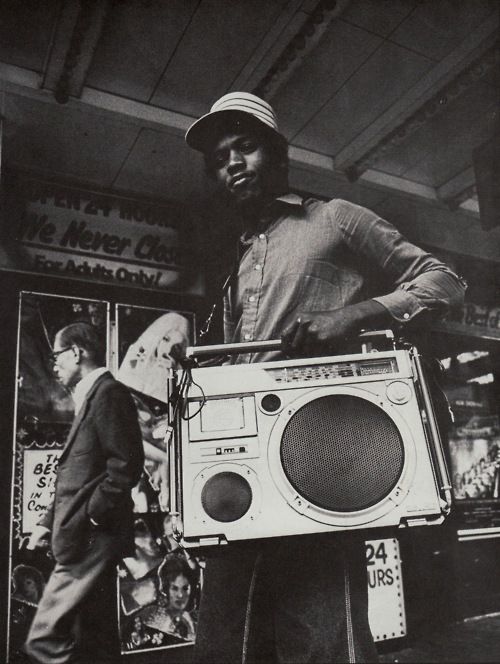 a man holding a boombox in front of a store sign with an advertisement on the wall behind him