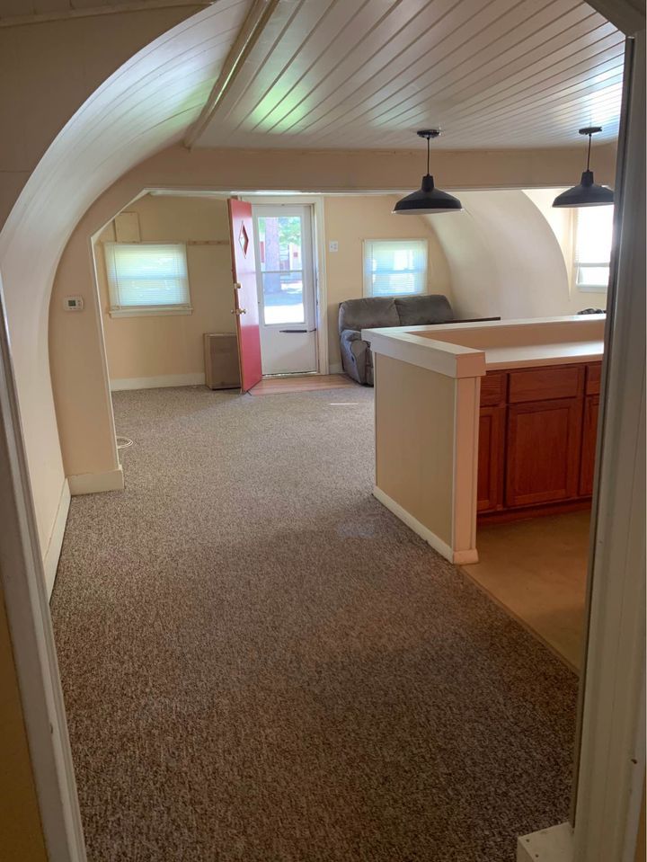 an open living room and kitchen area with wood cabinets, carpeted flooring and white walls