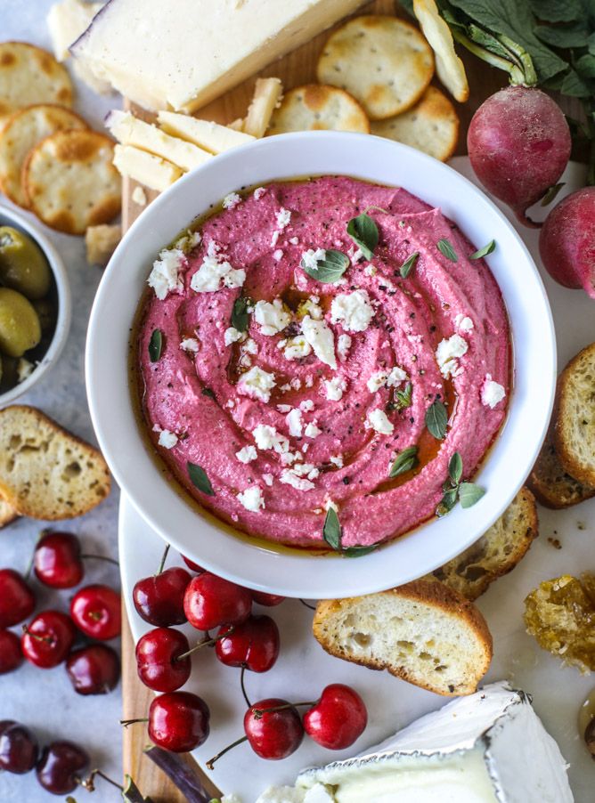 a white bowl filled with red dip surrounded by crackers, cherries and cheese