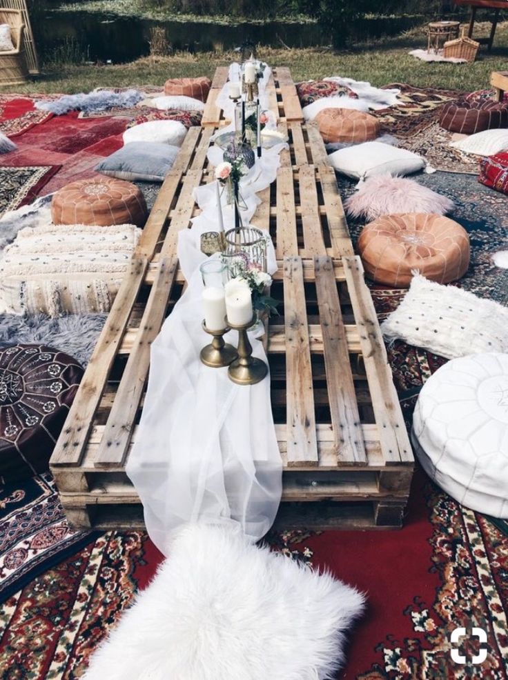 a table made out of wooden pallets with candles and blankets around it on the ground