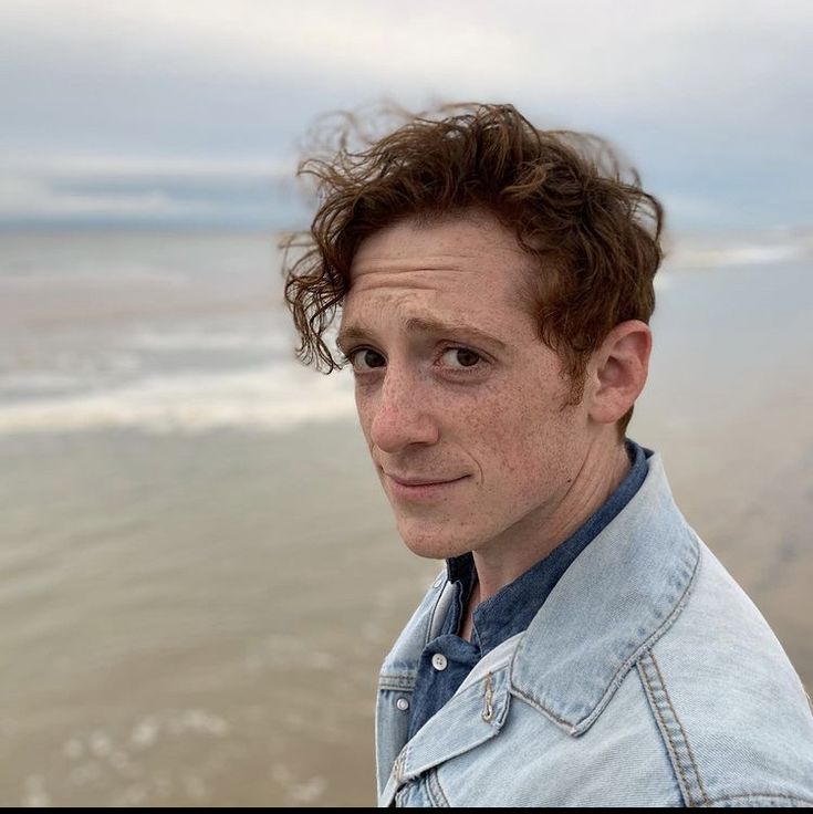 a man with curly hair standing on the beach