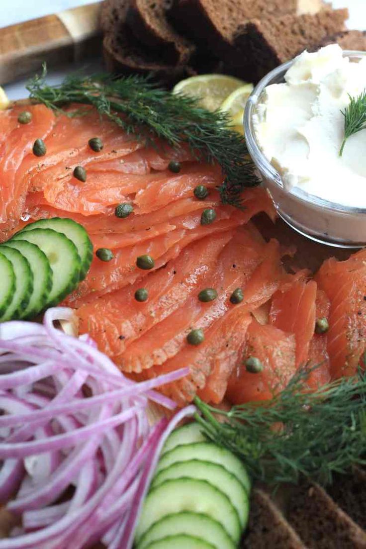 a platter with salmon, cucumbers, onions and sour cream on it