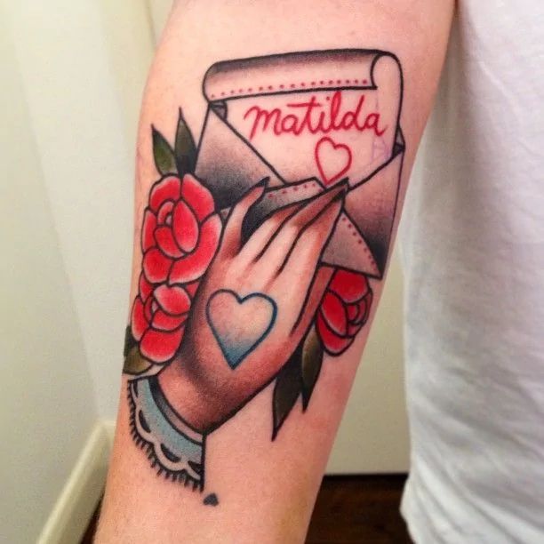 a woman's arm with a tattoo on it that says matilda and is holding a envelope