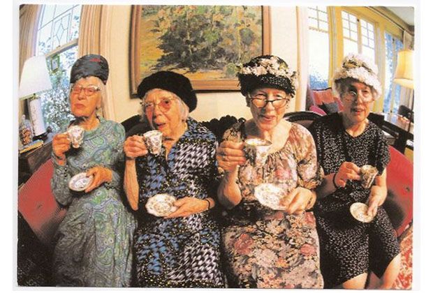 three older women sitting next to each other holding tea cups and looking at the camera