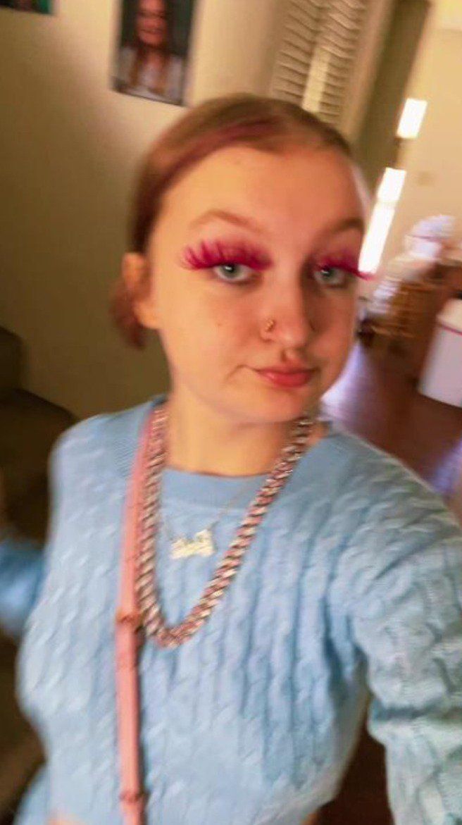 a woman with pink eyeliners is taking a selfie while wearing a blue sweater