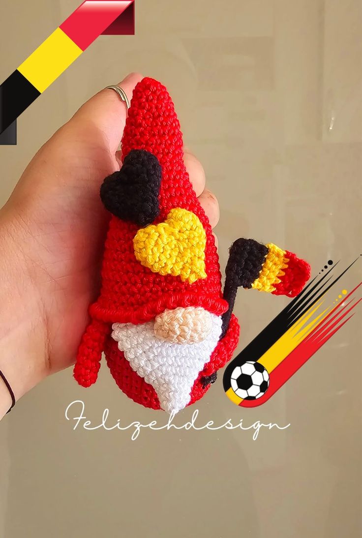 a hand holding a small crocheted red bird ornament with yellow, white and black feathers