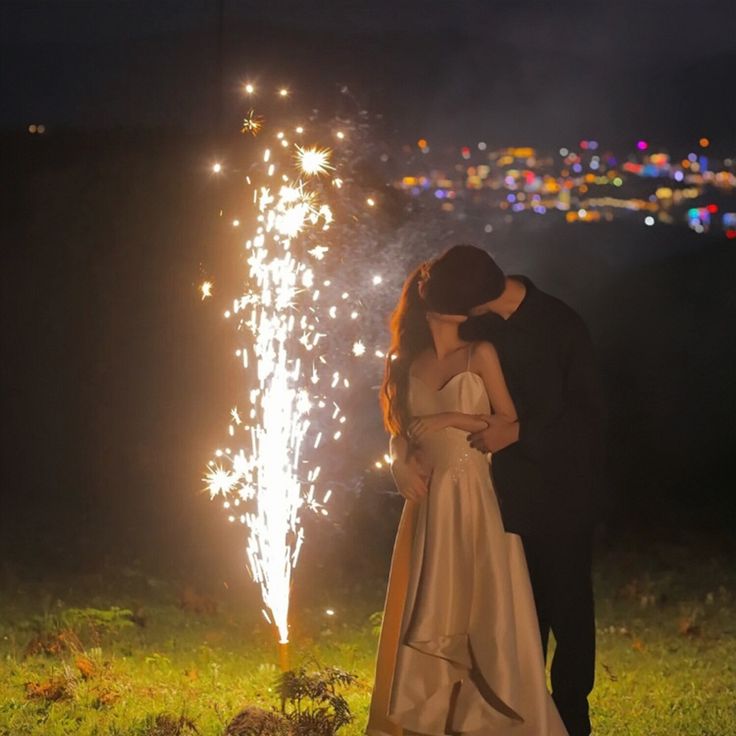 a bride and groom kissing with fireworks in the background