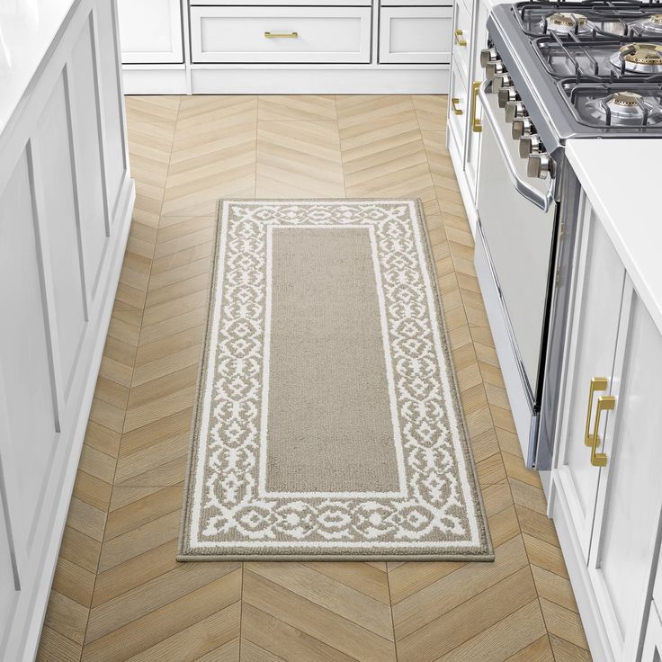 a kitchen with white cabinets and wood flooring next to an area rug on the floor