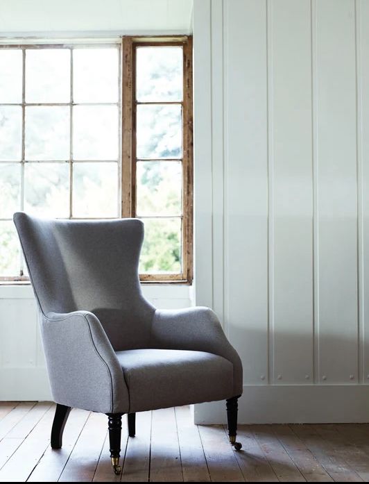 a gray chair sitting in front of a window next to a wooden floor and white walls