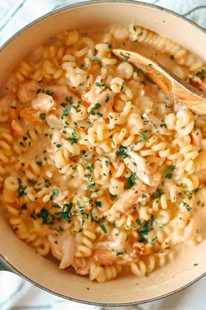 pasta with chicken and parsley in a skillet on a white tablecloth next to a wooden spoon