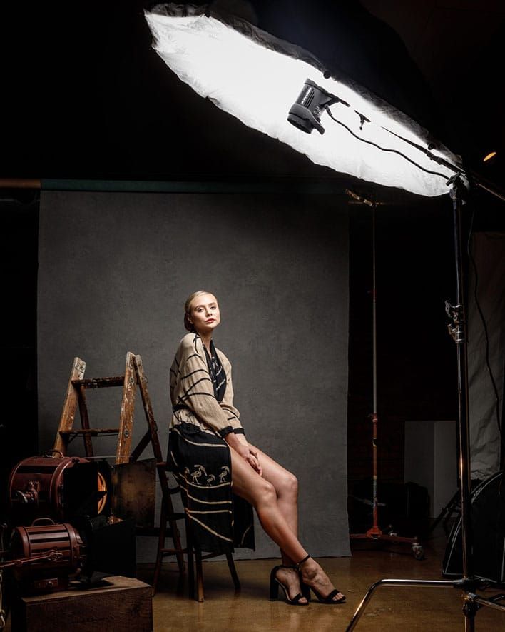 a woman sitting on a chair in front of a camera and lighting equipment with her legs crossed