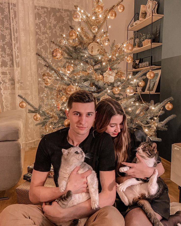 a man and woman holding two cats in front of a christmas tree