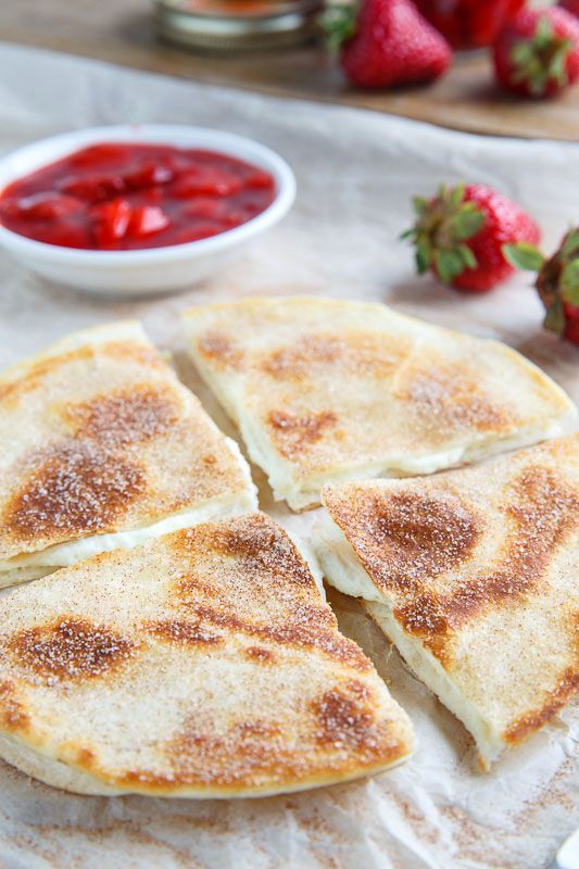 four slices of quesadilla sitting on top of a white napkin next to strawberries