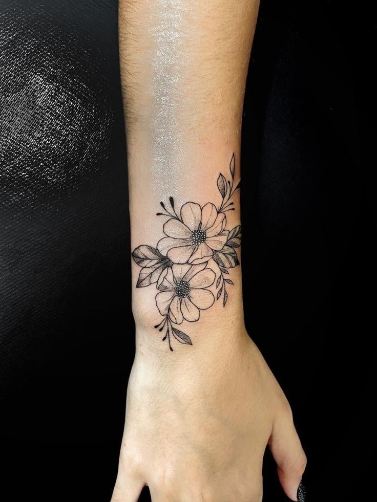 a woman's hand with a flower tattoo on her left wrist and black ink