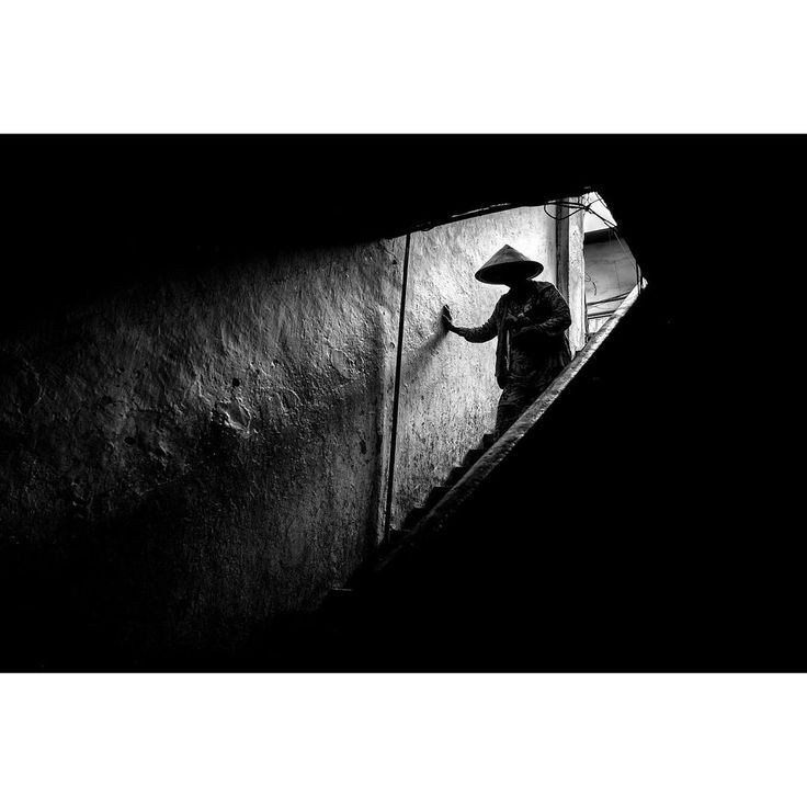 black and white photograph of a man climbing up the stairs with a straw hat on his head