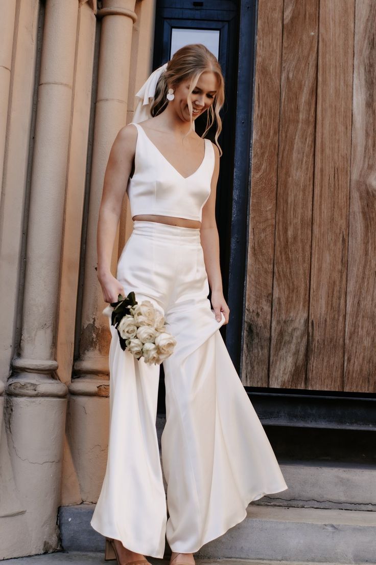 a woman in a white wedding dress is standing on the steps and holding a bouquet