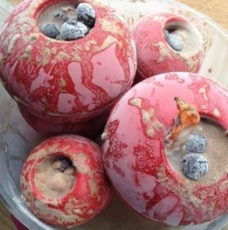 three red donuts with blueberries in them sitting on a plate covered in dirt