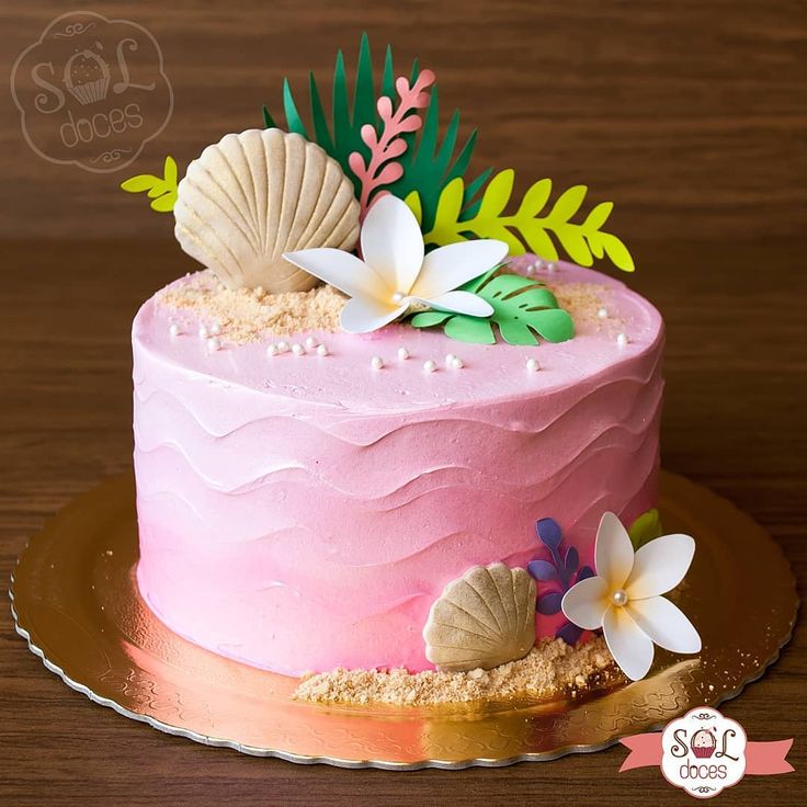 a pink cake decorated with flowers and seashells